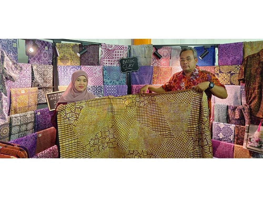Mohamad Rizan (kanan) menunjukkan batik tanah liat yang diusahakan oleh Nur Nabihah Zakaria sempena Festival Kraf Perak 2023 di Dataran Menara Condong, Teluk Intan, Perak.  
