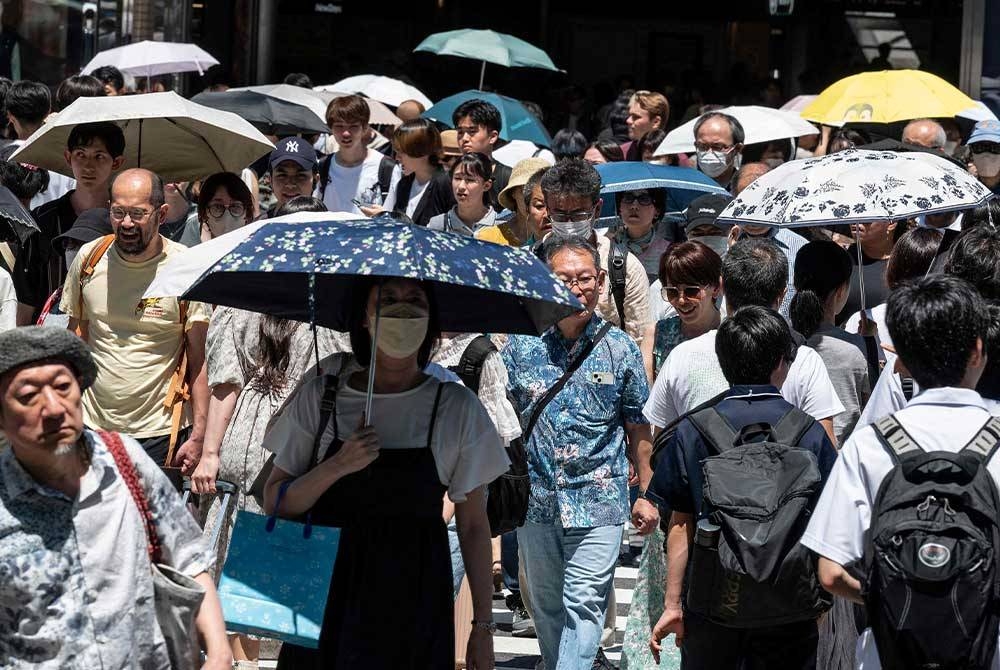 Foto yang diambil pada 30 Julai 2023 menunjukkan orang ramai menggunakan payung semasa berjalan di luar stesen Shinjuku berikutan suhu mencecah 35 darjah celcius. - Foto AFP