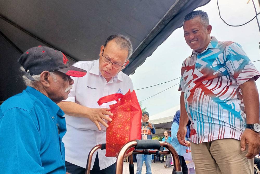 Abdul Fattah (tengah) bersama Fakhrul Razi menyantuni bekas peneroka, N Mulan, 76, sempena Karnival Usahawan Kami Anak Felda (KAF) Wilayah Trolak di Felda Trolak Utara dekat Sungkai pada Jumaat.