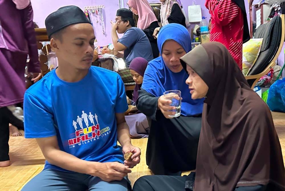 Anak-anak membantu memberikan minuman kepada ibu mereka, Robiah (kanan).