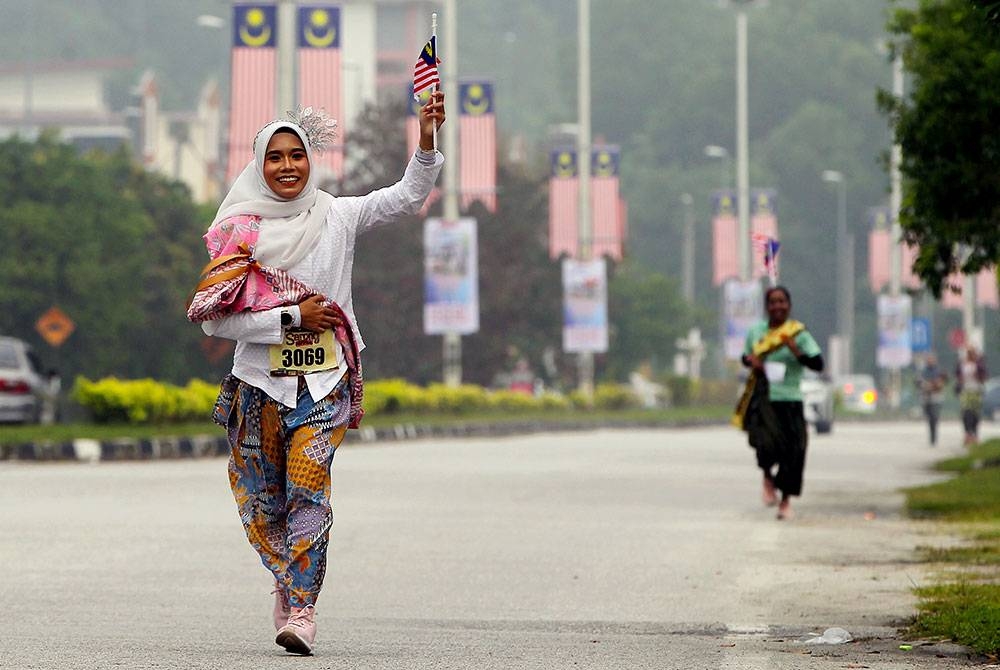 Peserta Farah Nur Ain Abdul Latif, 33, (kiri) bersemangat menyertai acara Sarong Run pada program Sarong Festival di Bulatan Sultan Azlan Shah hari ini.