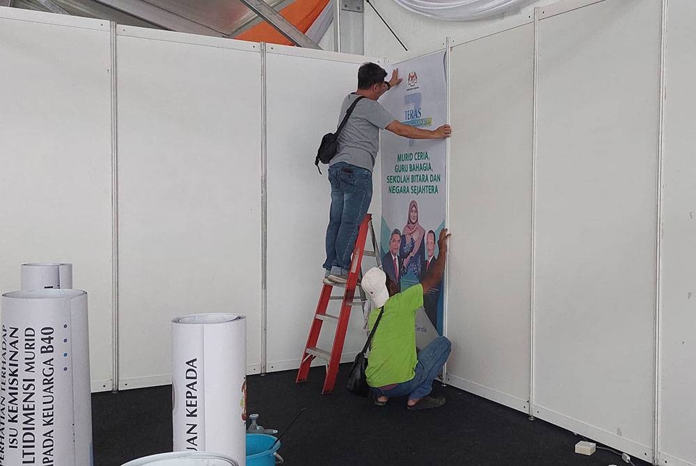 Pekerja memasang kertas dinding di tapak Karnival Pendidikan Sinar Bestari.