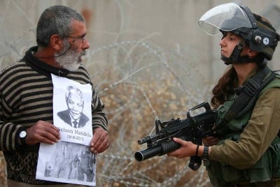 Aktivis pro-Palestin membawa potret bekas Presiden Afrika Selatan dan mangsa aparteid, mendiang Nelson Mandela semasa membantah pembinaan tembok pemisah di perkampungan Bilin, Tebing Barat. - Foto Agensi