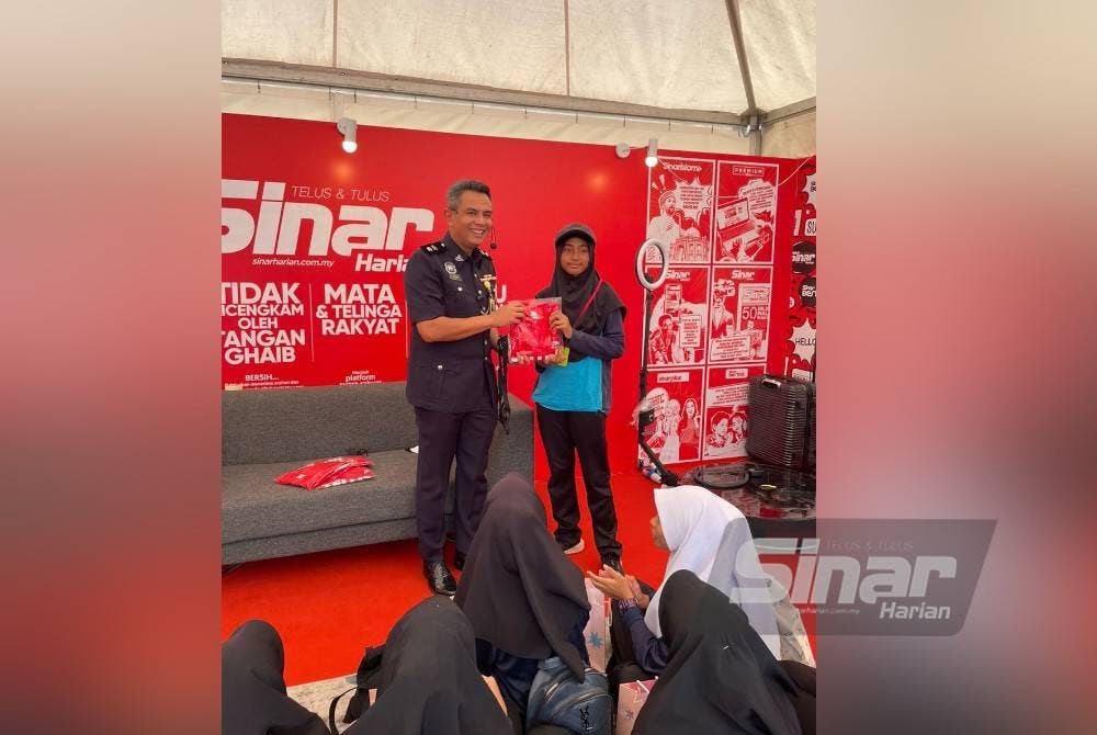 Muhamad Sajidan menyampaikan cenderamata kepada wakil pelajar Sekolah Kebangsaan Sungai Ramal Dalam selepas sesi temu wartawan di booth Sinar Harian di Karnival Pendidikan Sinar Bestari di Kompleks Karangkraf, Shah Alam pada Jumaat.