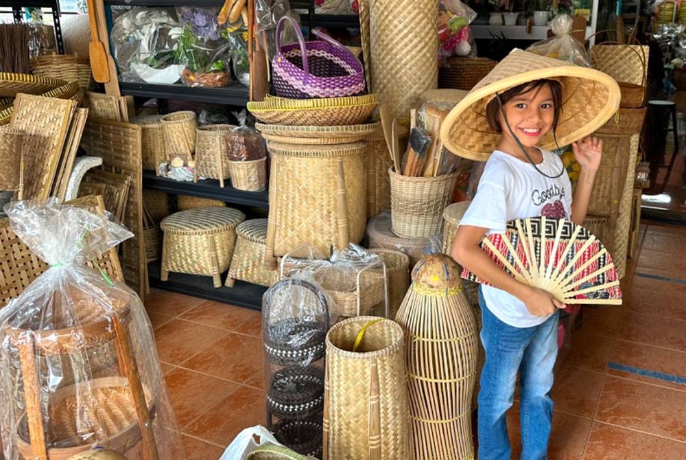 Seorang kanak-kanak mengayakan kipas tangan dan topi yang dihasilkan daripada buluh.