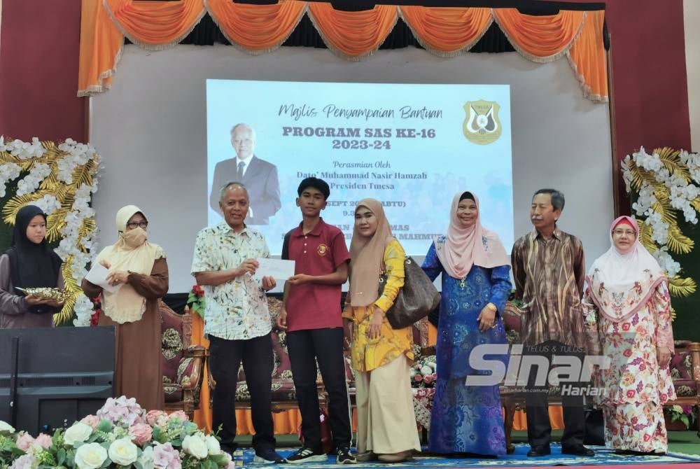 Muhammad Nasir (tiga dari kiri) menyerahkan sumbangan kepada pelajar sempena majlis penyampaian bantuan program 'Sponsor A Student' (SAS) kali ke-16 di Dewan Jubli Sekolah Menengah Kebangsaan Tengku Mahmud, Besut pada Sabtu.