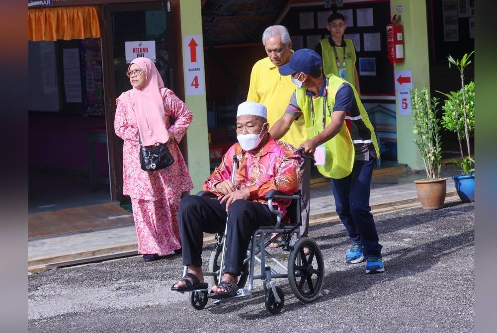 Md Noor yang berkerusi roda dibantu petugas SPR selepas menunaikan tanggungjawab mengundi di Sekolah Jenis Kebangsaan (Cina) Pei Chai pada Sabtu. - Foto Bernama
