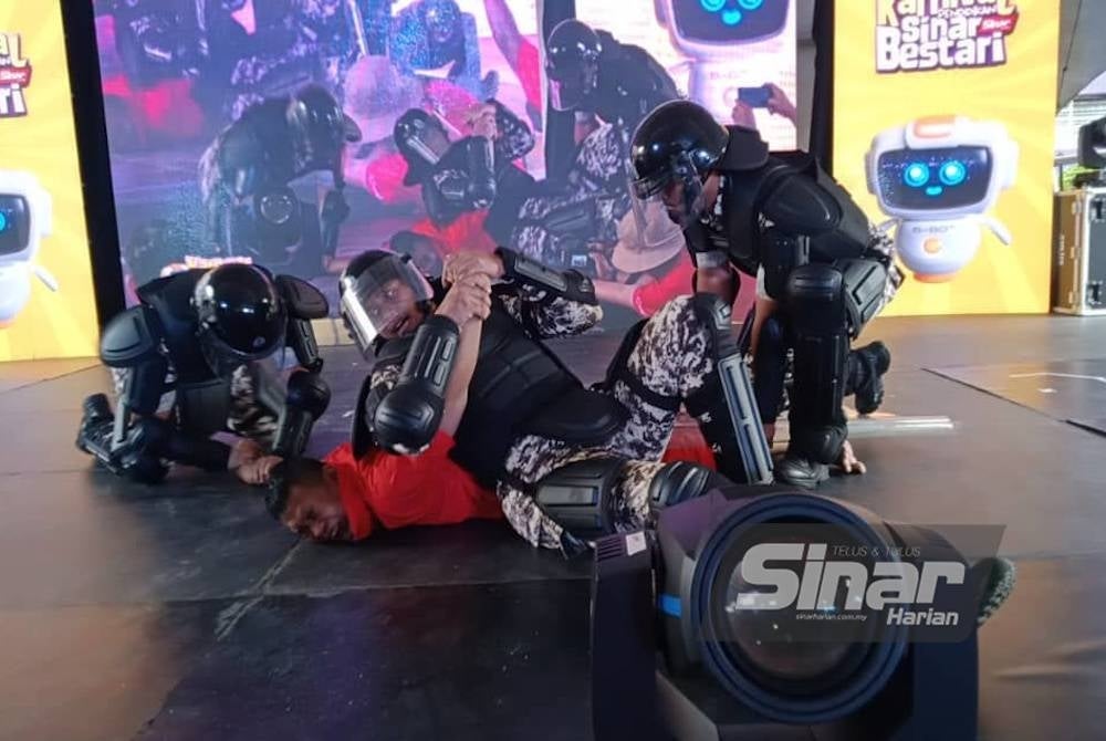 Aksi Ahmad Yusof (tengah) ketika melakonkan watak sebagai banduan yang ditenangkan oleh anggota Unit Kawalan Pencegahan Jabatan Penjara Malaysia di Karnival Pendidikan Sinar Bestari pada Sabtu.