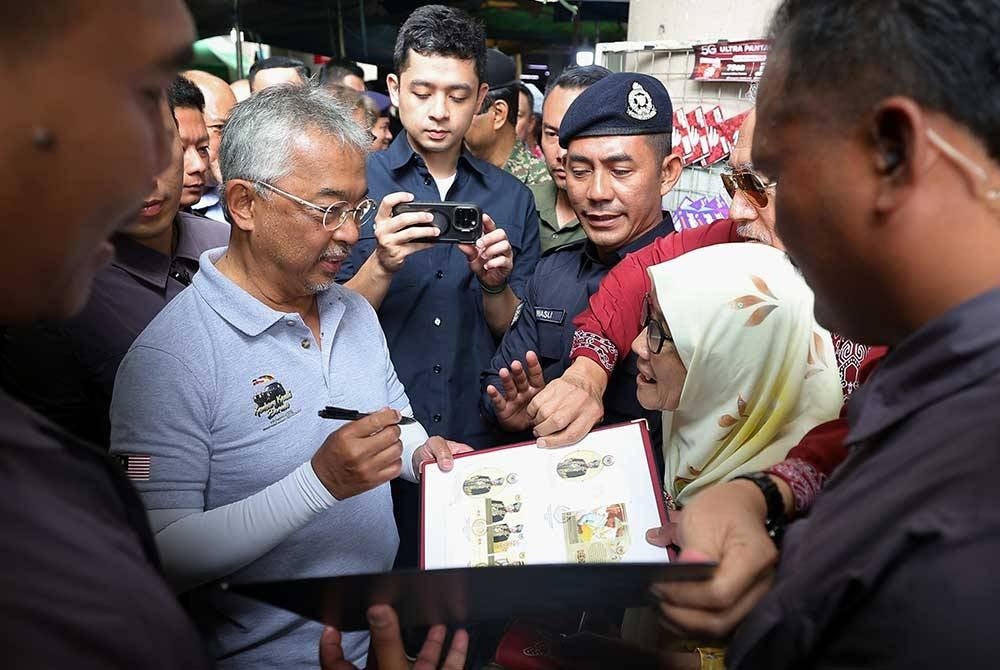 Yang di-Pertuan Agong Al-Sultan Abdullah Ri'ayatuddin Al-Mustafa Billah Shah berkenan menandatangan buku koleksi setem ketika membuat lawatan ke Pasar Sentral Sibu sempena Kembara Kenali Borneo . - Foto Bernama.