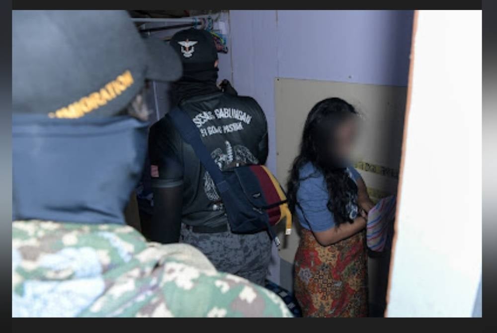 Dua anggota petugas memeriksa seorang warga asing semasa melakukan serbuan di Puncak Alam, Selangor pada Sabtu.