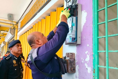 Wan Mohd Zahari (kanan) menyaksikan kakitangan TNB membuat operasi pemotongan bekalan elektrik di sebuah premis perniagaan di Cenderawasih pada Khamis.