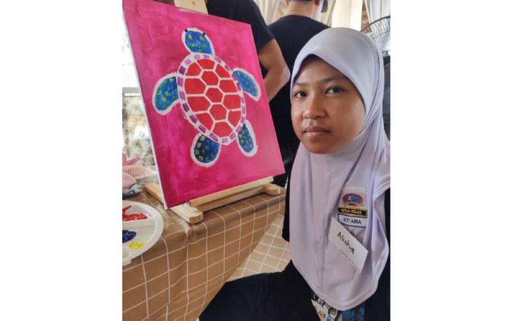Siti Aina Alisha Muhammad Izzuan, pelajar masalah pendengaran dari PPKI Sekolah Kebangsaan Seri Bayu teruja menunjukkan hasil seninya.