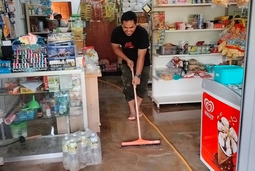 Muhamad Amirul membersihkan kedai runcit miliknya di Kampung Charuk Akar Mukim Tawar yang dinaiki air pada Khamis.