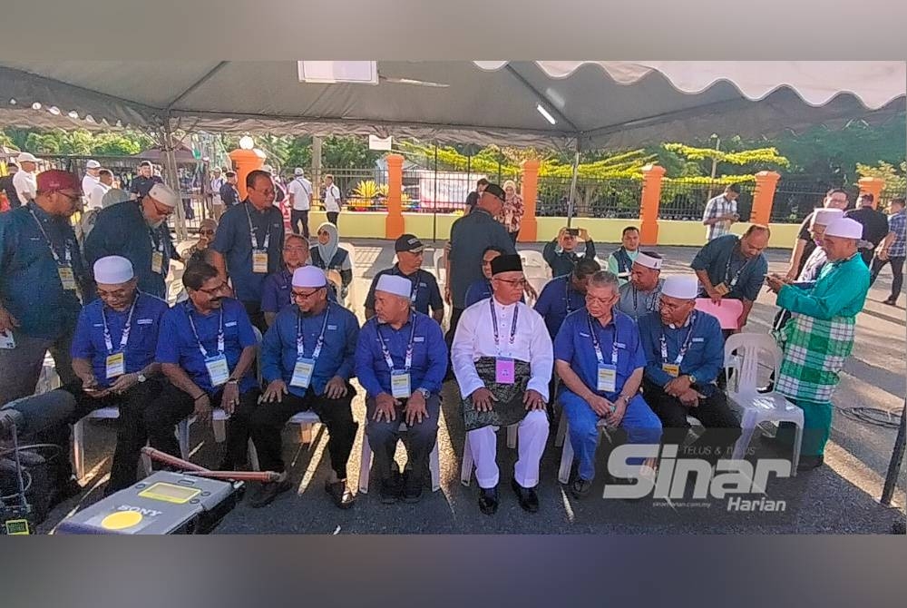 Cikgu Kasim (duduk, tiga dari kanan) ditemani pemimpin tertinggi PN menunggu di bawah khemah di luar Dewan Orang Ramai Felda Kemasul bagi proses pendaftaran nama sebagai calon pada Sabtu