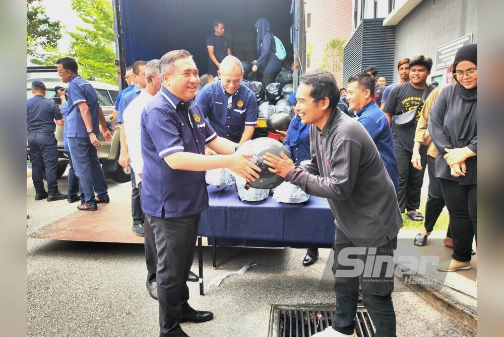 Anthony (kiri) menyerahkan topi keledar percuma kepada orang ramai yang hadir menukar topi keledar baharu.