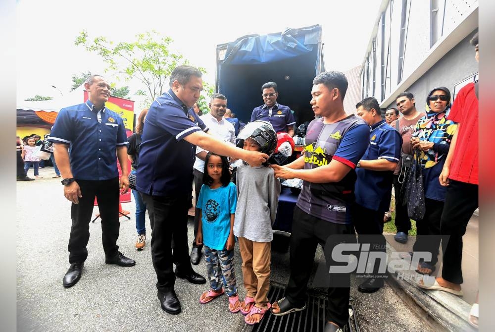 Anthony memakaikan topi keledar kepada seorang kanak-kanak sambil diperhatikan bapanya (kanan).