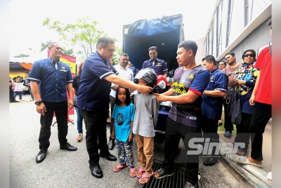 Anthony memakaikan topi keledar kepada seorang kanak-kanak sambil diperhatikan bapanya (kanan).