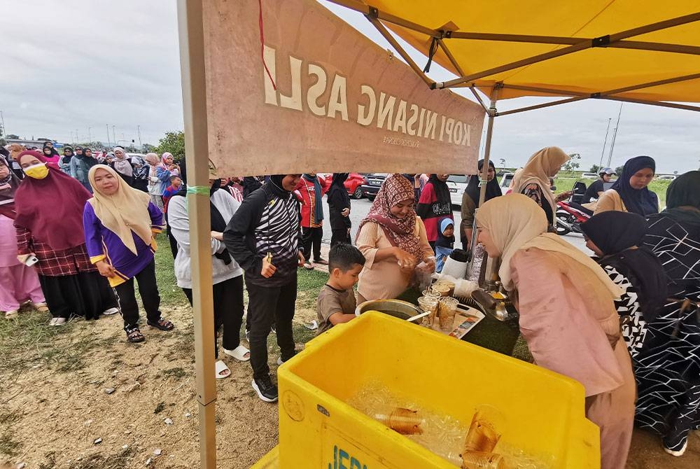 Nur Nadirah Syuhadah (kanan) melayani orang ramai yang ingin mendapatkan kopi di gerai Kopi Nisang Asli di jambatan angkat, Kuala Terengganu pada petang Ahad.