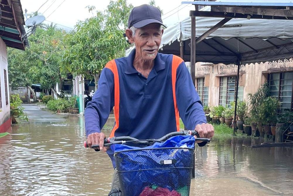 Abu Hassan mengayuh basikalnya meredah banjir untuk membeli makanan di kedai berhampiran.