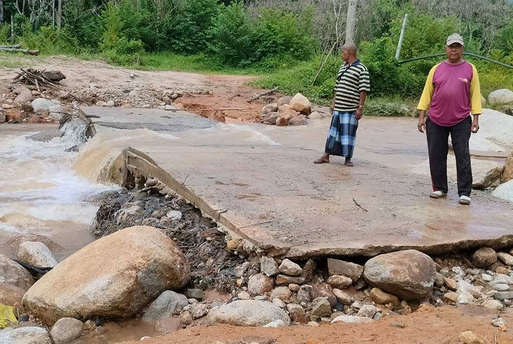 Ishak dan Mohd Yusof (kanan) menunjukkan titi yang dibina secara gotong-royong runtuh semula selepas seminggu siap akibat dilanda arus deras.