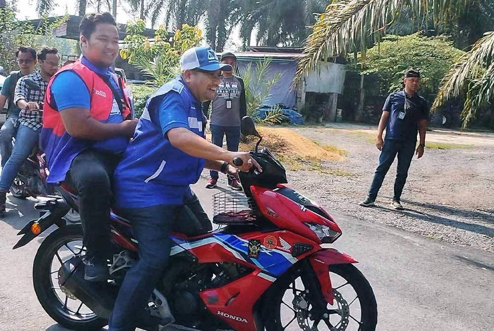 Amizar menunggang motosikal bersama jentera parti ketika menyantuni penduduk di Kampung Chemomoi, pada Jumaat.