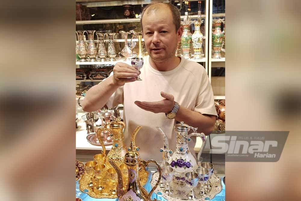 Seorang peniaga Uighur menunjukkan seni pertukangan tangan yang dijual di kedainya.