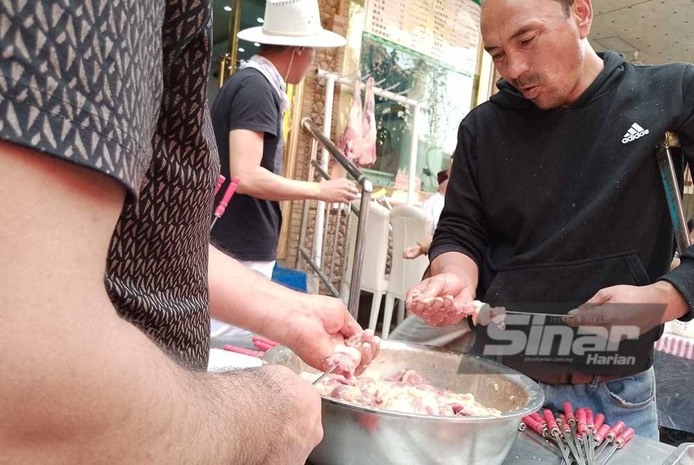 Dua pekerja sedang menyediakan kebab kambing di sebuah restoran halal di kota purba Kashgar.