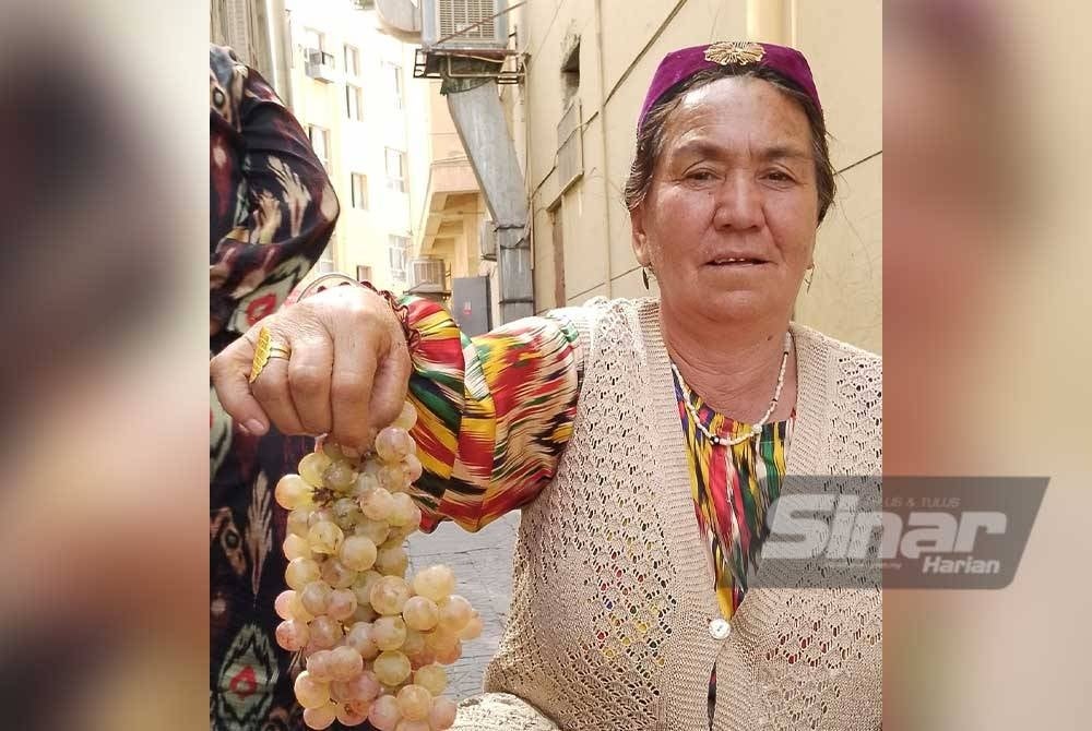 Seorang wanita Uighur menunjukkan buah anggur segar yang dijual di kawasan kaki lima.