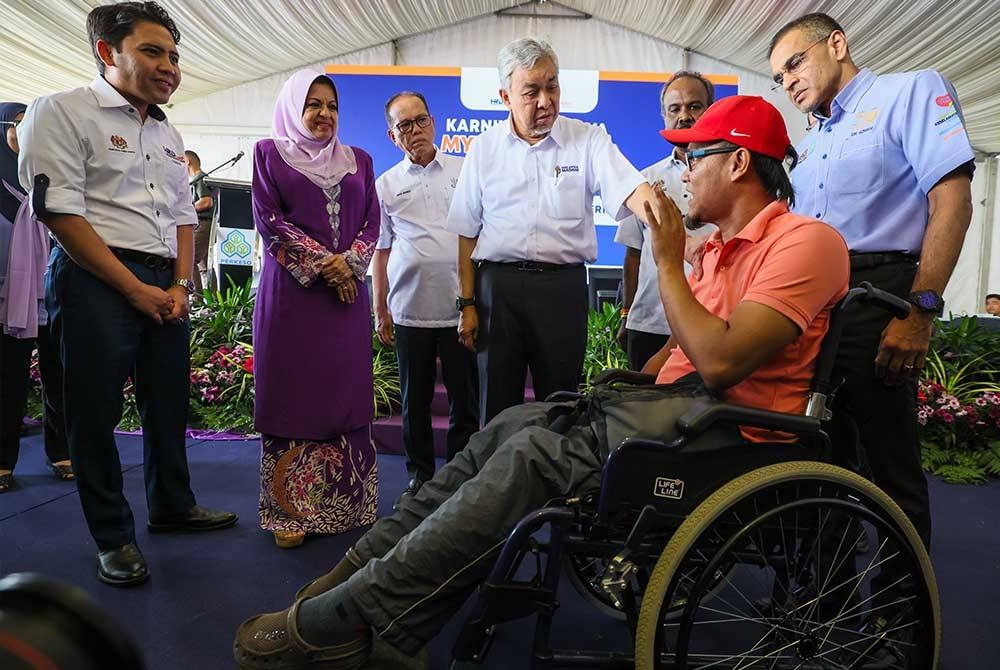 Ahmad Zahid bertanya khabar penerima Faedah Pencen Ilat PERKESO, Muhammad Ferdaus Abdul Rahim (berkerusi roda) yang lumpuh separuh badan akibat kemalangan jalan raya pada Karnival Kerjaya MyFuture Jobs bersama HAWA Malaysia di Felda Chemomoi hari ini. Foto Bernama