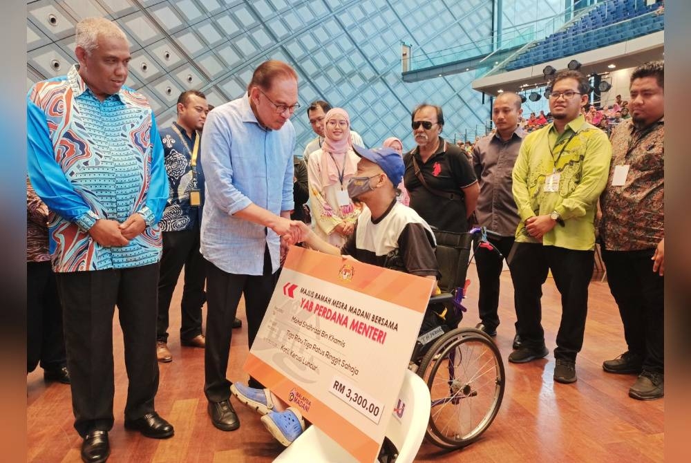 Anwar (dua dari kiri) menyampaikan bantuan e-Kasih kepada Mohd Shahrizal Khamis bagi bantuan katil dan kaki luncur berjumlah RM3,300 sempena Majlis Ramah Mesra Madani Di Dewan Cancelor UTP pada Ahad.