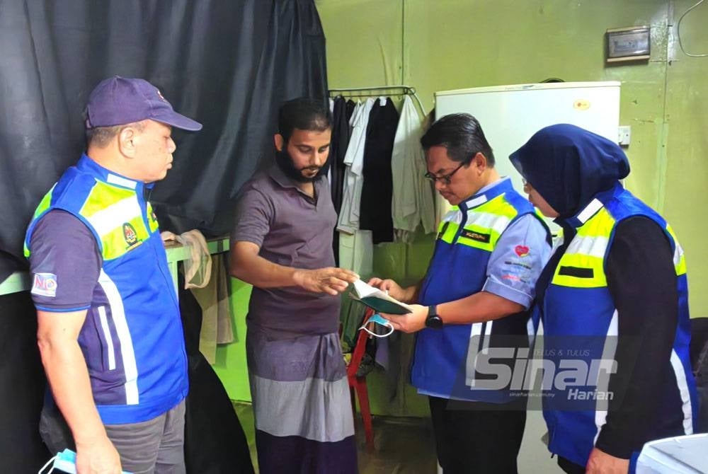 Mustapha (dua dari kanan) memeriksa dokumen seorang pekerja warga asing yang tinggal di asrama kontena.