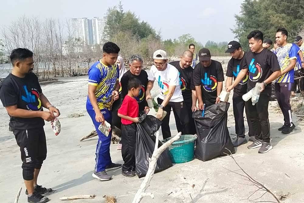 Razaman (empat dari kiri) bersama sebahagian peserta Program FitDOSM Perdana melakukan aktiviti pembersihan pantai di Taman Gelora pada Sabtu.