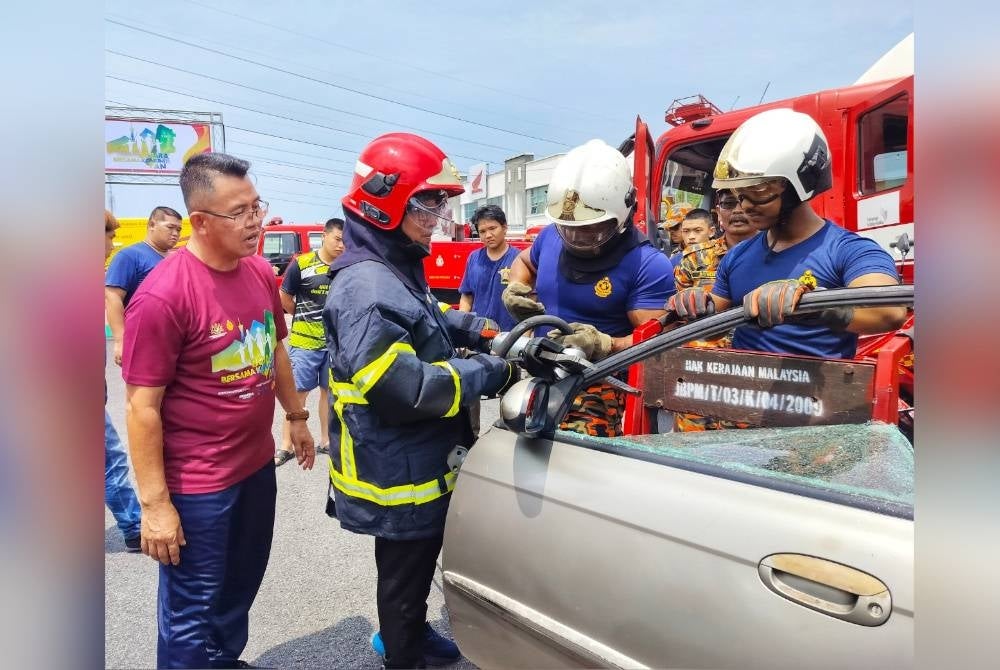 Awang Hidzel (kiri) melihat Yang Dipertua Majlis Daerah Yan, Mohamad Subhi Abdullah yang mencuba teknik mengepil pintu kereta di sudut pameran bomba.