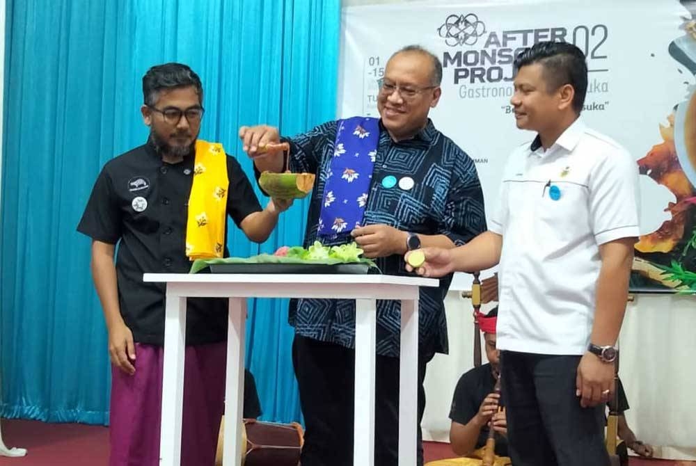 Amerudin (tengah) menuang budu ke dalam tempurung kelapa yang dipegang Azzahar sebagai simbolik perasmian Program After Monsoon Project 02, Gastronomi Langkasuka 'Bekwoh Langkasuka di sini pada Ahad.