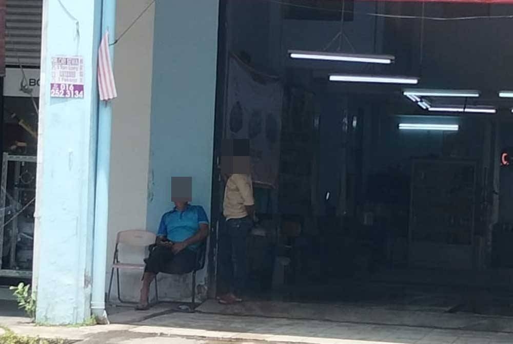 Dua pekerja warga asing di kedai cuci kereta sedang menunggu pelanggan.
