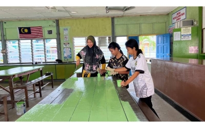 Seorang guru (kiri) bersama dua pelajar sedang mengecat meja sempena Program Gotong-Royong Madani yang diadakan sekolah mereka.
