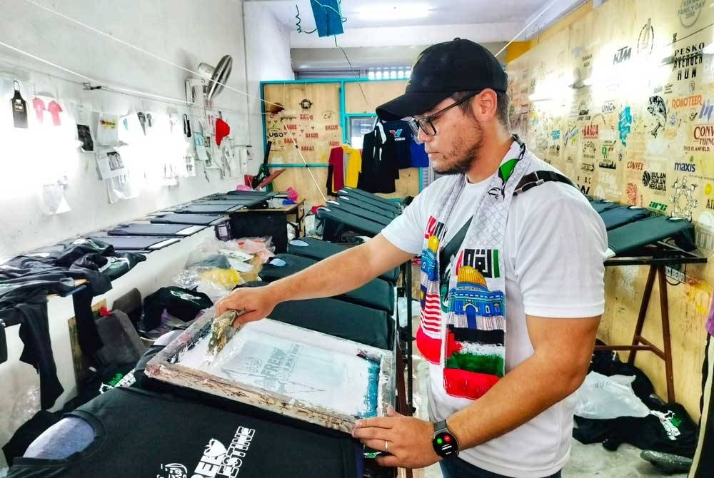 Ahmad Badiuzzaman sedang mencetak logo pada baju T di kilangnya di Alor Setar pada Ahad.