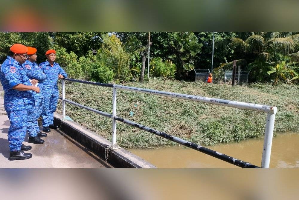 Zairil Anuar (tengah) memantau paras air sungai di lokasi banjir kilat di Kampung Bukit Belah, Sungai Petani pada Isnin.