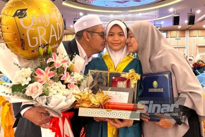 Izzah (tengah) menerima ciuman daripada ibu bapanya atas kejayaan yang diraih.