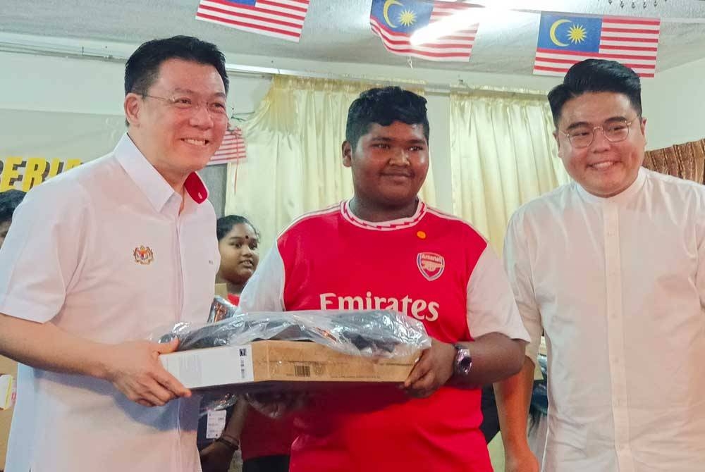 Kor Ming (kiri) dan ADUN Pasir Berdamar, Woo Kah Leong menyampaikan sumbangan komputer riba kepada salah seorang murid pada majlis di SJKT Sithambaram Pillay, Teluk Intan pada Sabtu.