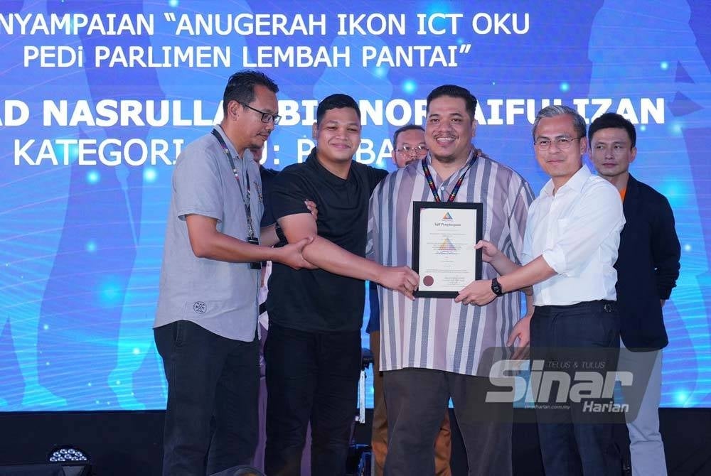 Fahmi (kanan) menyampaikan anugerah Ikon ICT OKU PEDi Parlimen Lembah Pantai kepada Muhammada Nasrullah Norsaifulizan pada Program Pemerkasaan OKU Celik Digital yang berlangsung di Pusat Komuniti IWK Eco Park pada Ahad. - Foto Sinar Harian / MOHD HALIM ABDUL WAHID.
