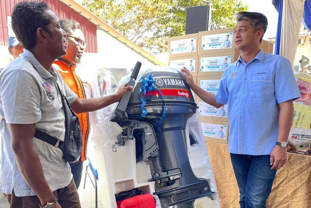 Muhammad Faiz (kanan) menyampaikan bantuan enjin bot kepada salah seorang nelayan pada Program Rahmah Mesra Madani Bersama Nelayan Pulau Pinang di Teluk Bahang pada Isnin.