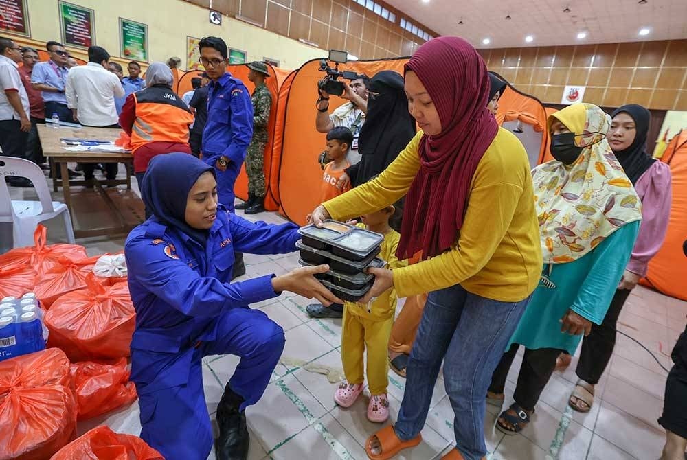 Anggota Angkatan Pertahanan Awam membantu mengagihkan makanan kepada mangsa banjir di PPS Sekolah Menengah Kebangsaan Dengkil. - Foto Bernama