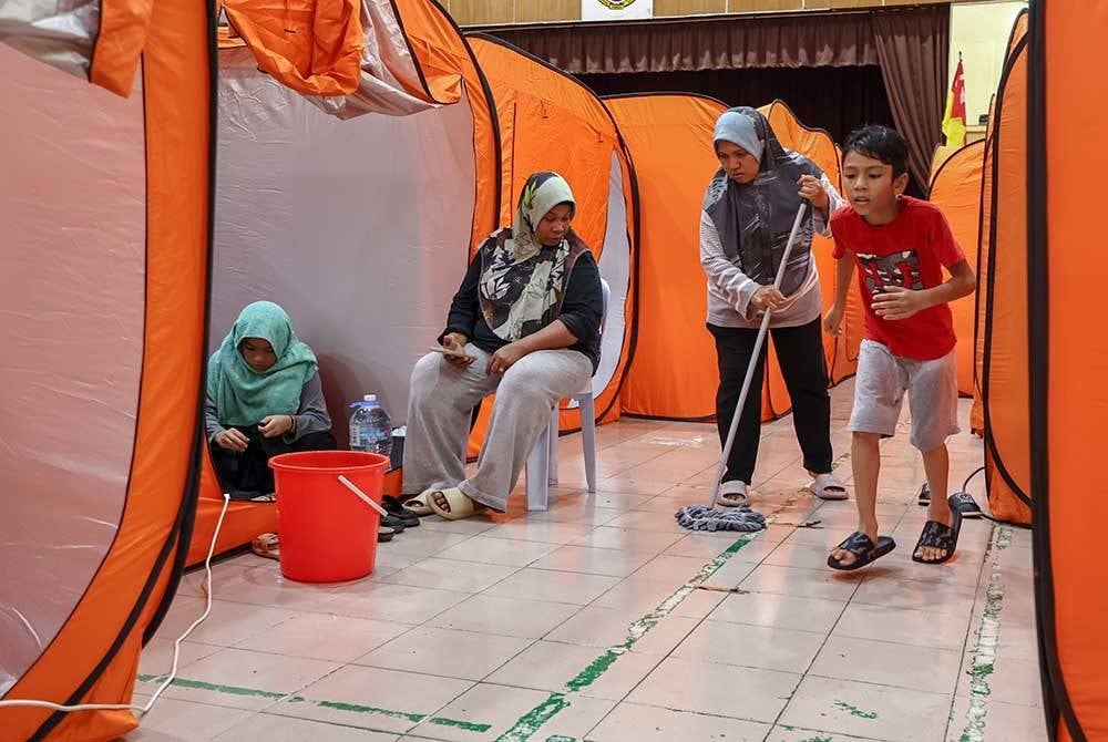 Mangsa banjir turut membantu membersihkan sekitar dewan di PPS Sekolah Menengah Kebangsaan Dengkil. - Foto Bernama