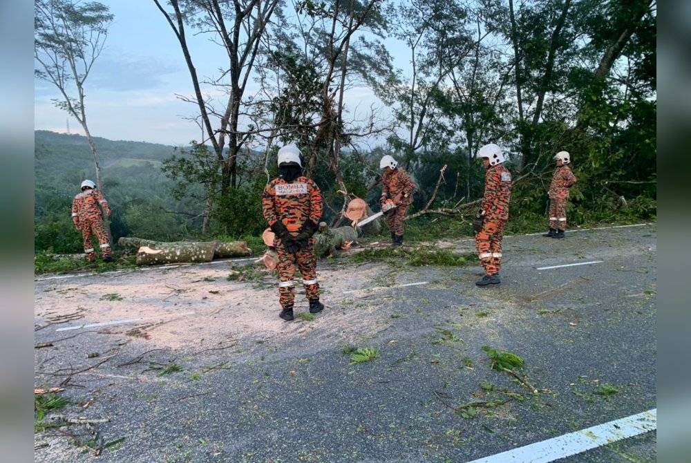 Anggota BBP Slim River membantu memotong pokok yang tumbang merentangi jalan di Felda Trolak Jaya, Slim River, pagi tadi. - Foto JBPM Perak