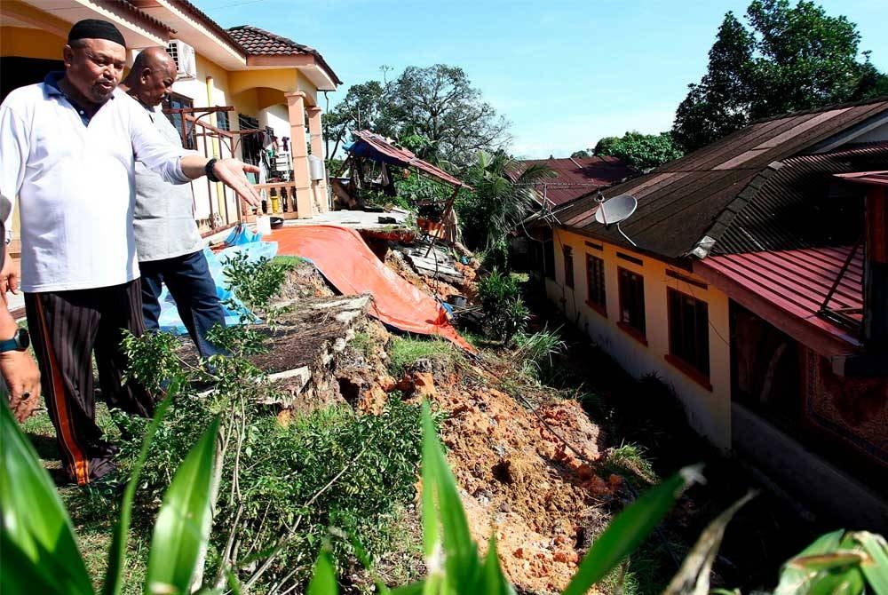 Zaidi (kiri) menunjukkan kesan runtuhan tebing dalam kejadian hujan lebat petang semalam di rumahnya di Kampung Dato Ahmad Said Tambahan Baru 1, Gugusan Manjoi. - Foto Bernama