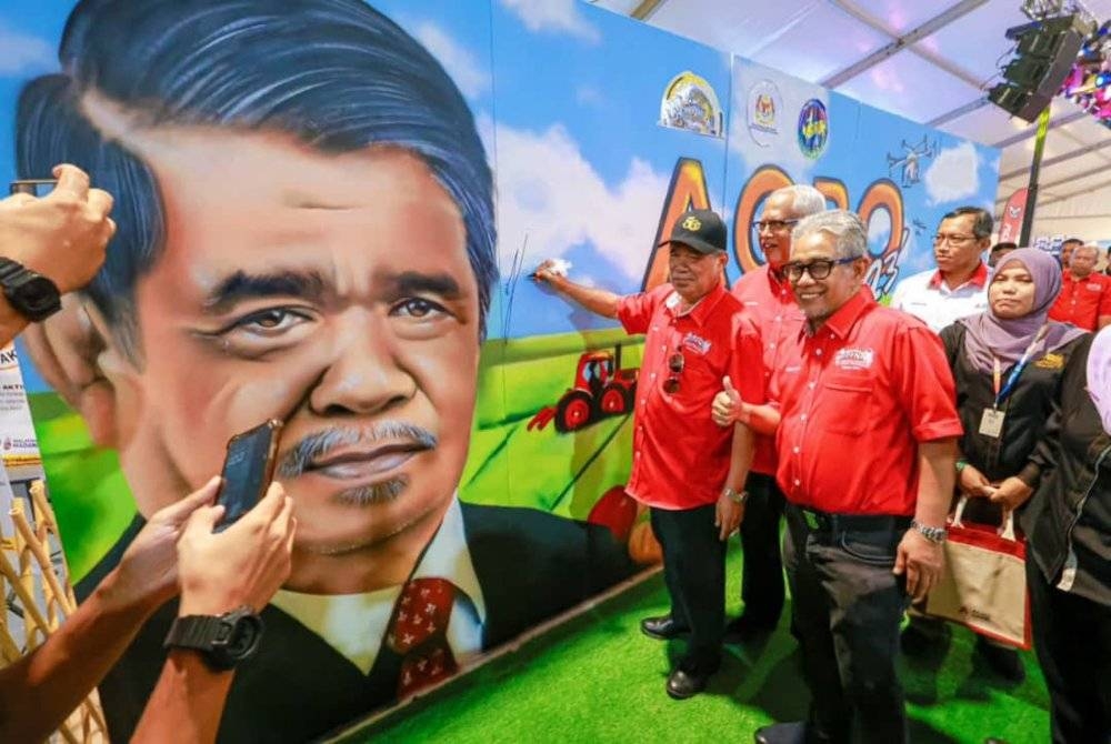 Mohamad (kiri) menandatangani potret beliau ketika hadir merasmikan Program Pembangunan Agropreneur Muda Siswazah sempena HPPNK 2023 di Bulatan Sultan Azlan Shah di Ipoh pada Sabtu.