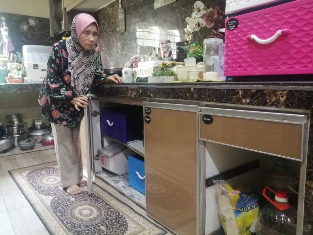 Noriah menunjukkan keadaan kabinet dapur yang lopong selepas pintunya dibuang selepas tidak boleh digunakan.