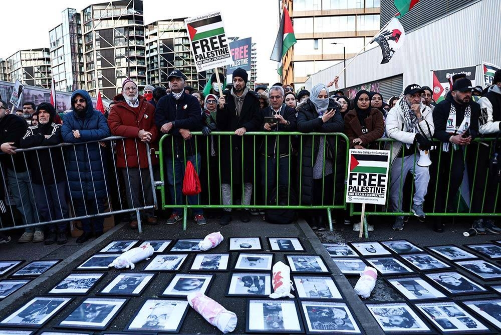 Penunjuk perasaan memegang sepanduk dan bendera di sekeliling tugu peringatan sementara dengan gambar mangsa pengeboman di Gaza, semasa 'Perarakan Kebangsaan Untuk Palestin' di tengah London pada Sabtu. - Foto: AFP