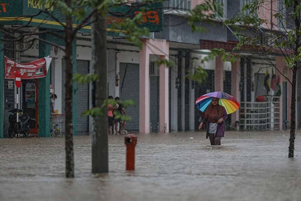 Penduduk D'Aman Meru Raya melintasi jalan yang dinaiki air ketika tinjauan di Meru Raya hari ini. - Foto Bernama